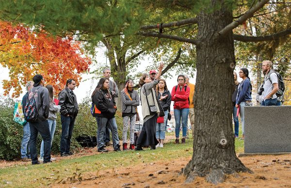 A class of students stand outside under a large tree