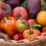 A selection of bell peppers and tomatoes in a round woven basket.