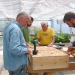 A group of men in a green house building a wooden box.