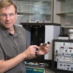 A man holding a small piece of equipment as he talks about it.