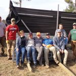 A group sitting on a large roll of wire fencing, smiling for the photo.