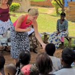 Two white women standing and walking in front of a group of Ugandans