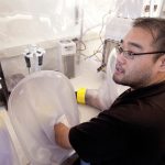 A man sitting at a lab table with his arm inside a transparent plastic oval