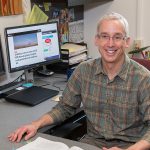 Bill Provencher sitting at his desk with graphics pulled up on his dual computer screens