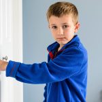 A young boy standing across from a door of a bedroom