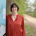 A woman leaned against a map on a wooded path