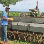 A man standing in front of a large piece of farming machinery at the edge of a field
