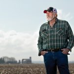 Mike Cerny posing with a field and farm in the distance behind him.