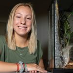 A girl smiling next to a tank that's holding a tarantula