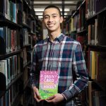 'Vỹ Lương', a freshman biochemistry major, photographed at UW–Madison's College Library with the book Green Card Youth Voices: Immigration Stories from Madison and Milwaukee High Schools, which contains his story. Photo by Michael P. King