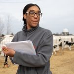 Rekia Salter stands, notebook in hand, in front of a row of Holstein calf hutches. Salter says her research is teaching her technical skills that will be invaluable when she goes to work as a consultant in the industry.