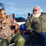 Two men in winter coats sitting together on a boat in Alaskan waters