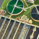 An aerial view of a facility. There are two large circular vats and large rows filled with water as well.