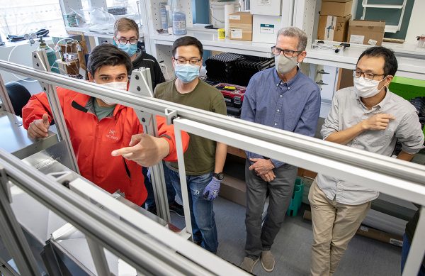 Men standing together in a lab, learning how to use machinery. 