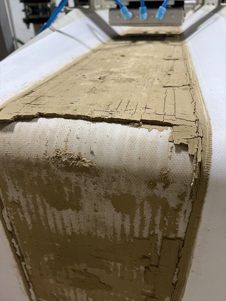 A conveyer belt coated in a thin layer of a clay-like material. 