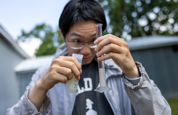 A close-up of a man measuring the amount of liquid in two vials in his hands.