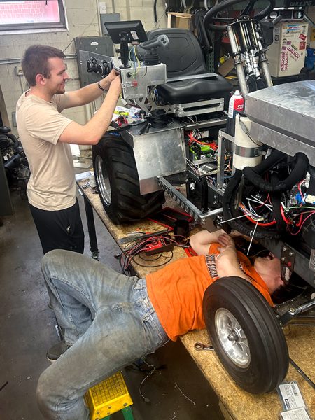 Two men working on their tractor in a shop.
