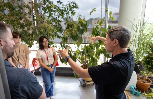 A professor speaks to students next to a tree.