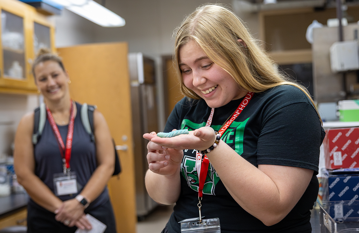 A student smiles as she holds a caterpillar in the palm of her hand