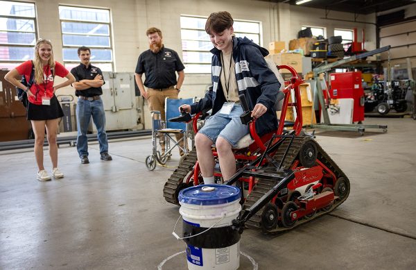 A student sits in a mechanical chair, lifting a bucket with the machinery.