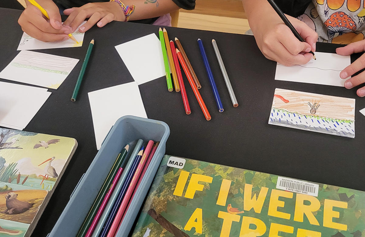 A close up of students using colored pencils to dram landscapes on notecards.
