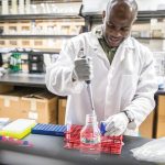 A scientist in a lab using a large pipet and test tubes