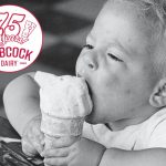 A black and white photo of a boy about two years old opening his mouth as wide as possible to take a bite out of a vanilla ice ceam scoop on top of a cake cone. A Babcock Dairy 75 Years circular logo is superimposed over the image in top left.