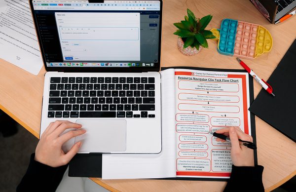 A birds eye view of a student sitting at a table working. The student has a laptop open and an informational guide notebook with resources. the student holds a writing utensil in their hand. 
