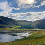 A landscape on a hilly wetland. There is a small lake at the foot of the large rolling hills in the background.