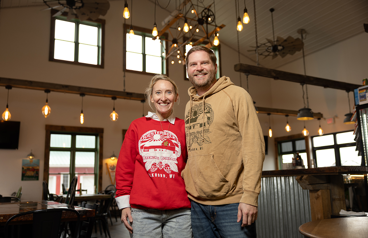 a man and woman standing next to each other, smiling. They are standing inside their business. There is a counter and tables behind them.