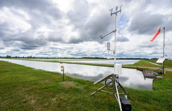 A metal tripod shaped machine stands in the grass next to a bog.